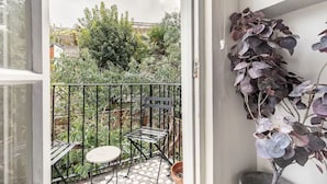A balcony with a metal chair and table, a potted plant, and a view of a garden with various plants and a fence.