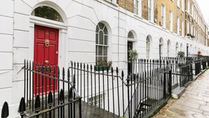 A row of white buildings with a red door, black iron fence, and a narrow sidewalk.