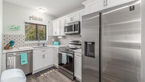 Una cocina moderna con armarios blancos, electrodomésticos de acero inoxidable y un ventanal con vistas a árboles.