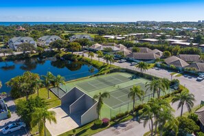 An aerial view of a residential area with houses, a tennis court, and a body of water.