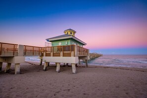 Una playa con un muelle de madera que conduce a un edificio verde con una torre, con vistas al océano.