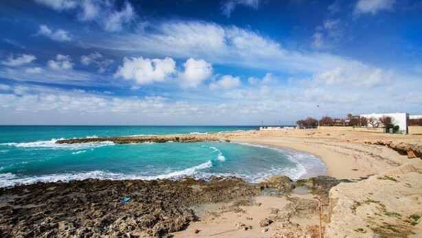 Une plage côtière avec un rivage rocheux, des zones sablonneuses et un ciel bleu dégagé.