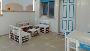 Une pièce avec un plafond blanc, une fenêtre bordée de bleu, une porte blanche également bordée de bleu, ainsi que plusieurs tables et bancs blancs.