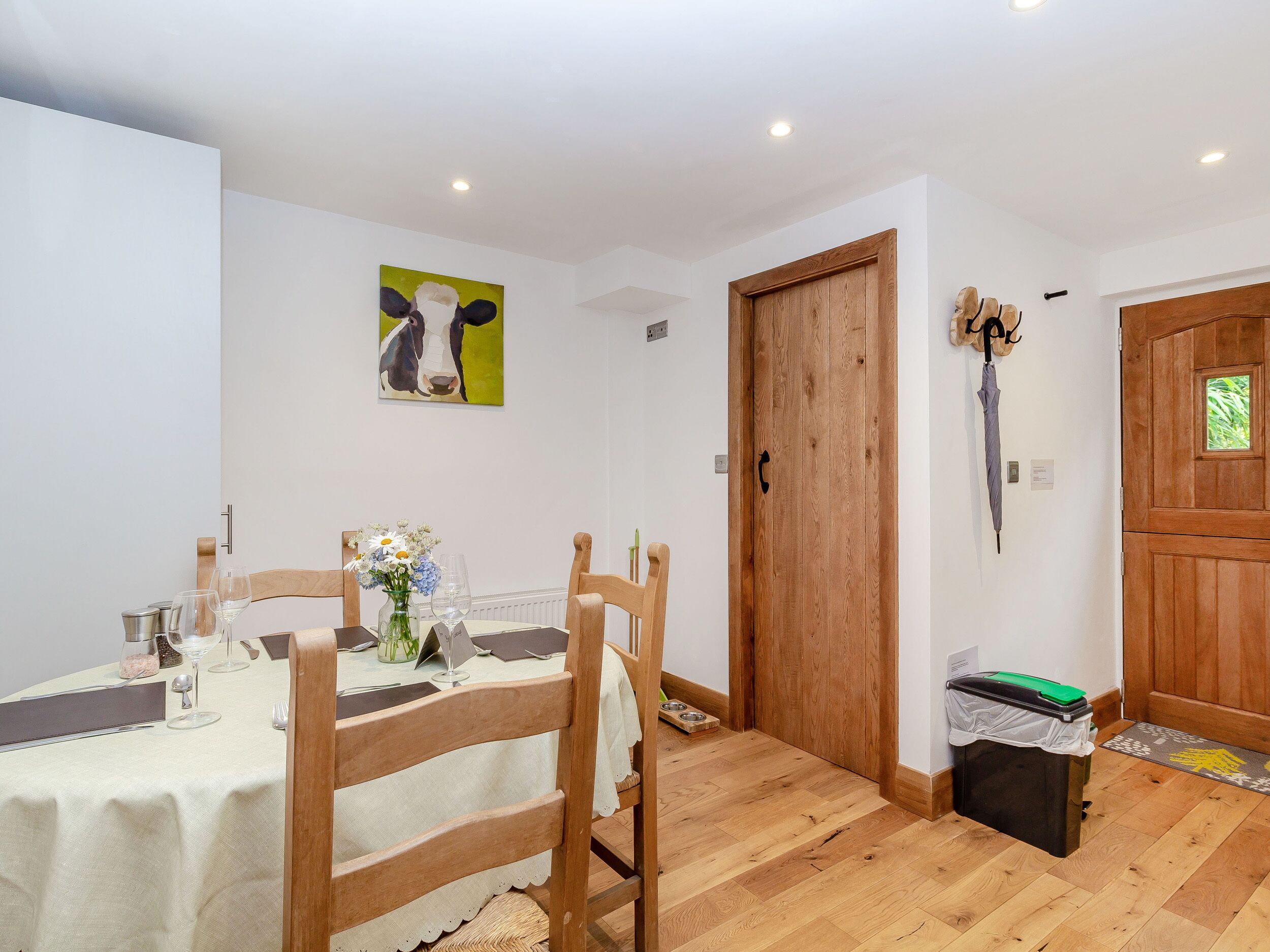 A dining area with a table set for two, a wooden chair, a vase with flowers, and a painting on the wall.