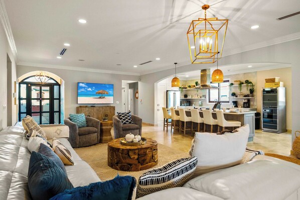 A spacious living room with a large sofa, a coffee table, and a television displaying a beach scene.