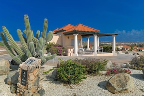 A building with a red-tiled roof, white columns, and a patio area with outdoor furniture. - Charming 5BR Pool Home w Patio near Beaches, Aruba (Noord)