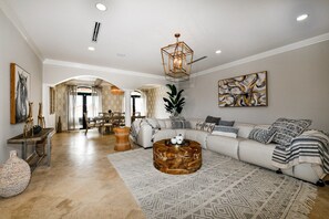 A spacious living room with a large sofa, a coffee table, and a chandelier.