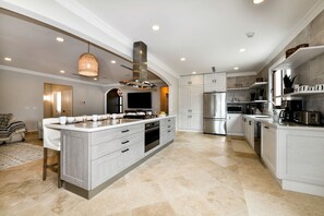 A spacious kitchen with a central island, stainless steel appliances, and a hanging light fixture. - Designer 6BR Pool Villa in Gated Tierra del Sol (Noord)