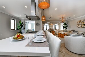 A modern kitchen with a dining area, featuring a long table set for four, a built-in oven, and a hanging light fixture.