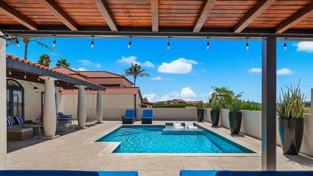 Un área de piscina en la azotea con sillones de descanso, piscina y terraza cubierta.