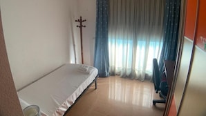 A small, sparsely furnished room with a single bed, a desk, and a chair.