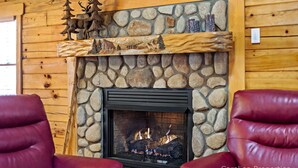 A stone fireplace with a fire, surrounded by wooden walls and a mantel with decorative figures. - Hot Tub, Mirror Lake Access, Fireplace - Outlander Cabin by Carolina Properties (Lake Lure)