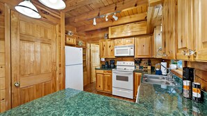 A kitchen with wooden cabinets, a white refrigerator, a stove, and a microwave. - Hot Tub, Mirror Lake Access, Fireplace - Outlander Cabin by Carolina Properties (Lake Lure)