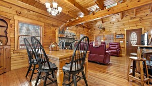 A wooden cabin interior with a dining table, chairs, a sofa, and a fireplace. - Hot Tub, Mirror Lake Access, Fireplace - Outlander Cabin by Carolina Properties (Lake Lure)