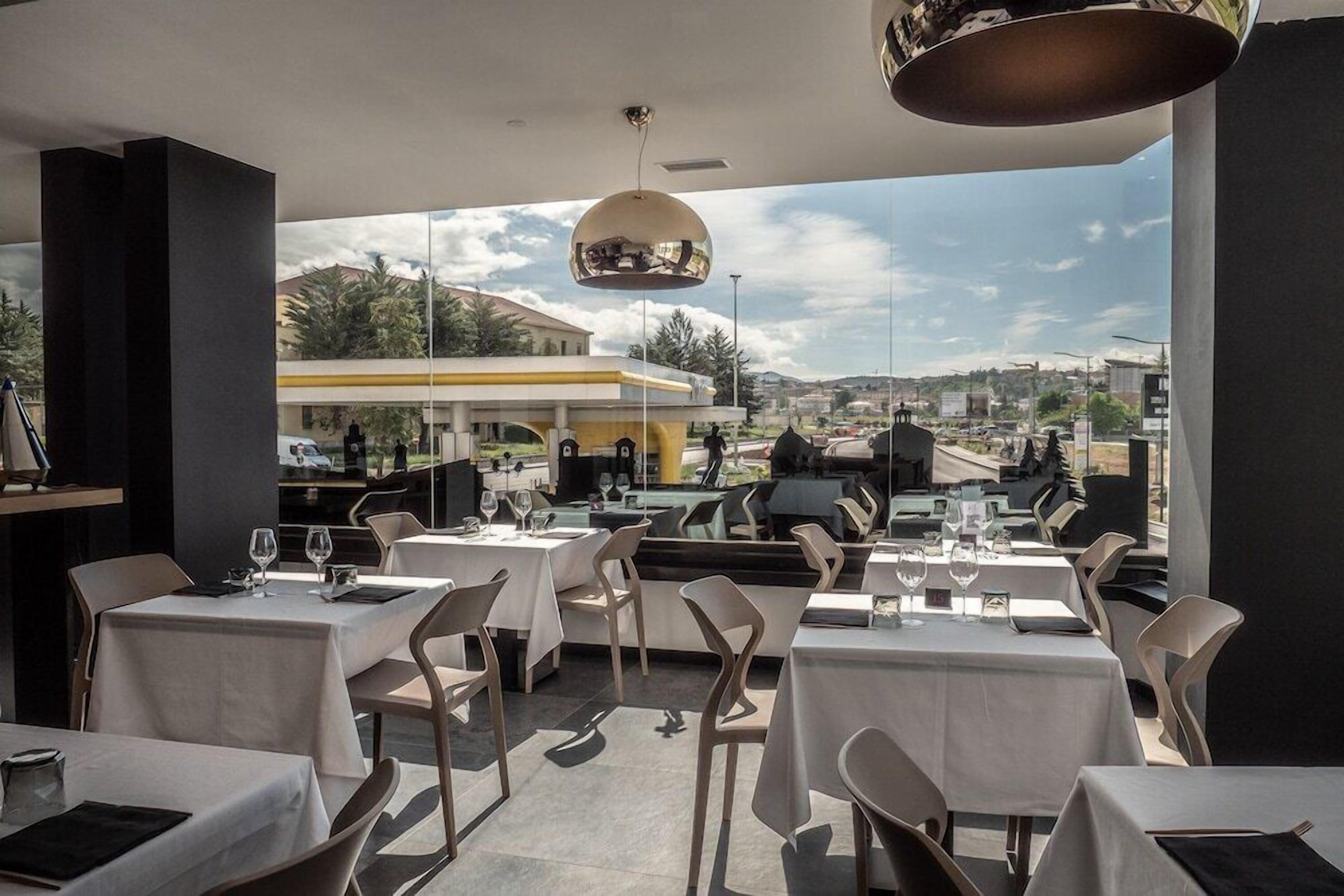 Un espace de restauration en plein air avec des tables et des chaises, une vue sur le paysage urbain et un grand luminaire suspendu.