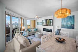 A modern living room with a large TV, comfortable seating, and a view of the outside. - Indies 101 | Modern Corner Beach Condo | Spacious Balcony Retreat (Gulf Shores)