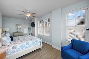 A bedroom with a bed, a ceiling fan, a TV, and a window with blinds. - Indies 101 | Modern Corner Beach Condo | Spacious Balcony Retreat (Gulf Shores)
