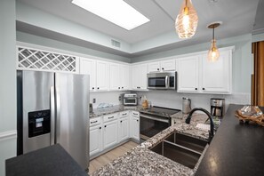 A modern kitchen with white cabinetry, stainless steel appliances, a granite countertop, and pendant lighting. - Indies 101 | Modern Corner Beach Condo | Spacious Balcony Retreat (Gulf Shores)