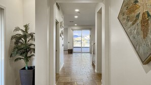 A hallway with a potted plant, a large painting, and a view through a glass door to an outdoor area. - The Lakefront Social: An Extraordinary Waterfront Experience (Indio)