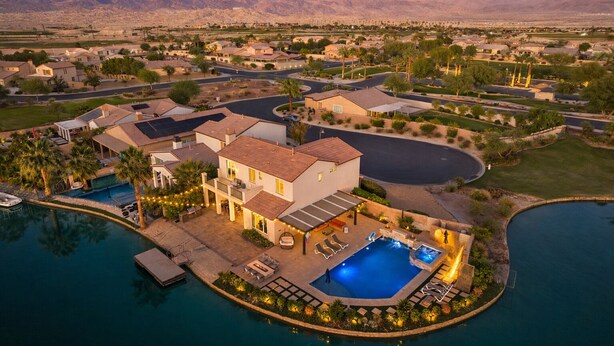 A large house with a swimming pool, surrounded by a landscaped garden and a view of mountains. - The Lakefront Social: An Extraordinary Waterfront Experience (Indio)
