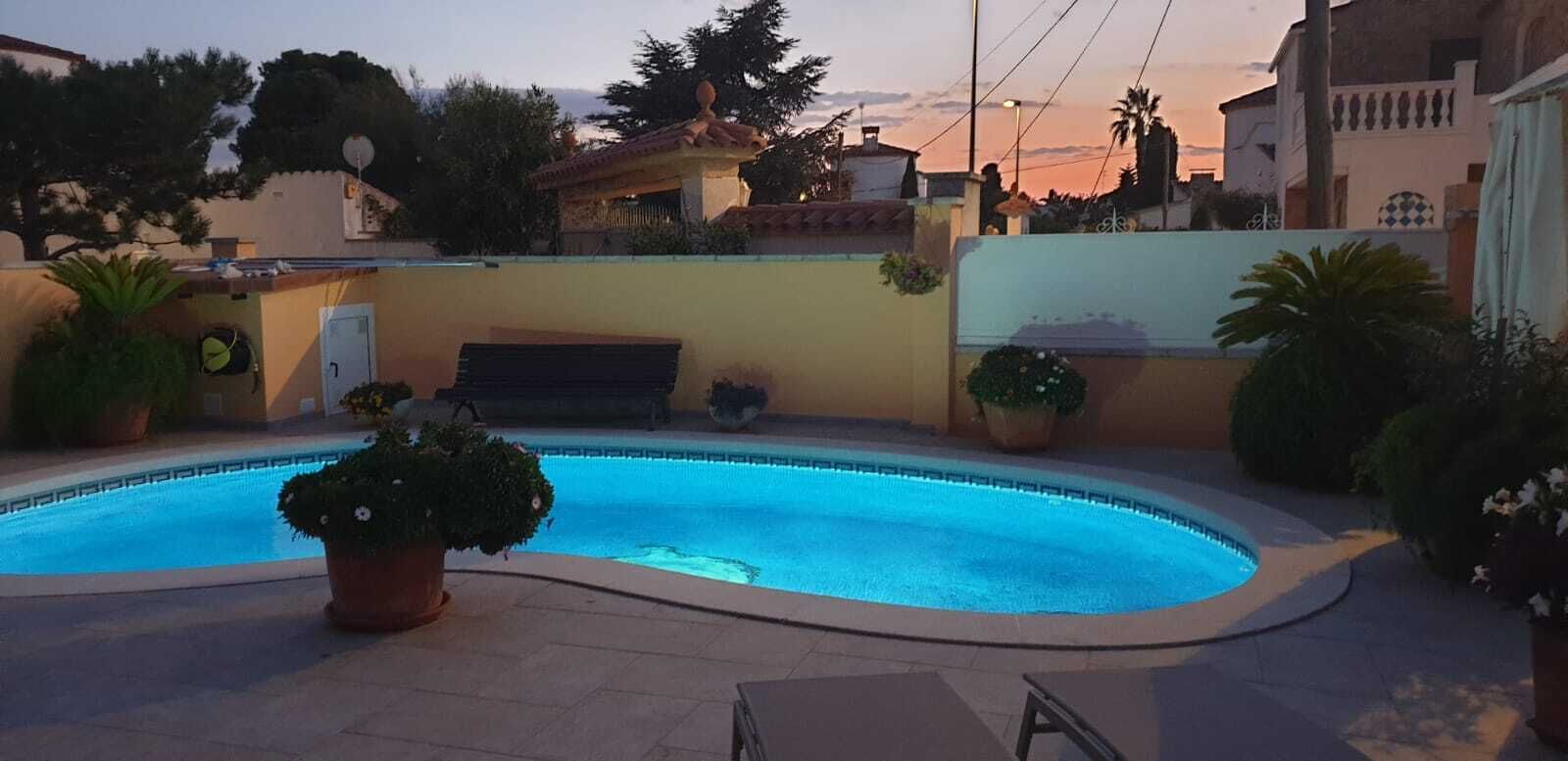 Une piscine à bord incurvé, entourée de plantes en pot et agrémentée d’un banc.