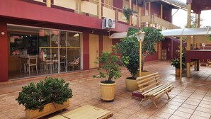 Un espacio al aire libre con patio, mobiliario para sentarse, plantas en macetas y un edificio de fachada roja con detalles amarillos.