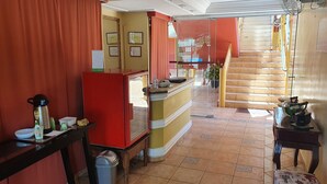 Un vestíbulo de hotel con un mostrador de recepción, un refrigerador rojo, un calendario y una escalera que lleva a un piso superior.