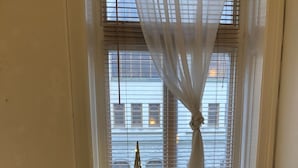 A dining area with a round table and four chairs, a decorative candle, and a window with blinds and a curtain. - Stockholm Central Apartment 911 (Stockholm)