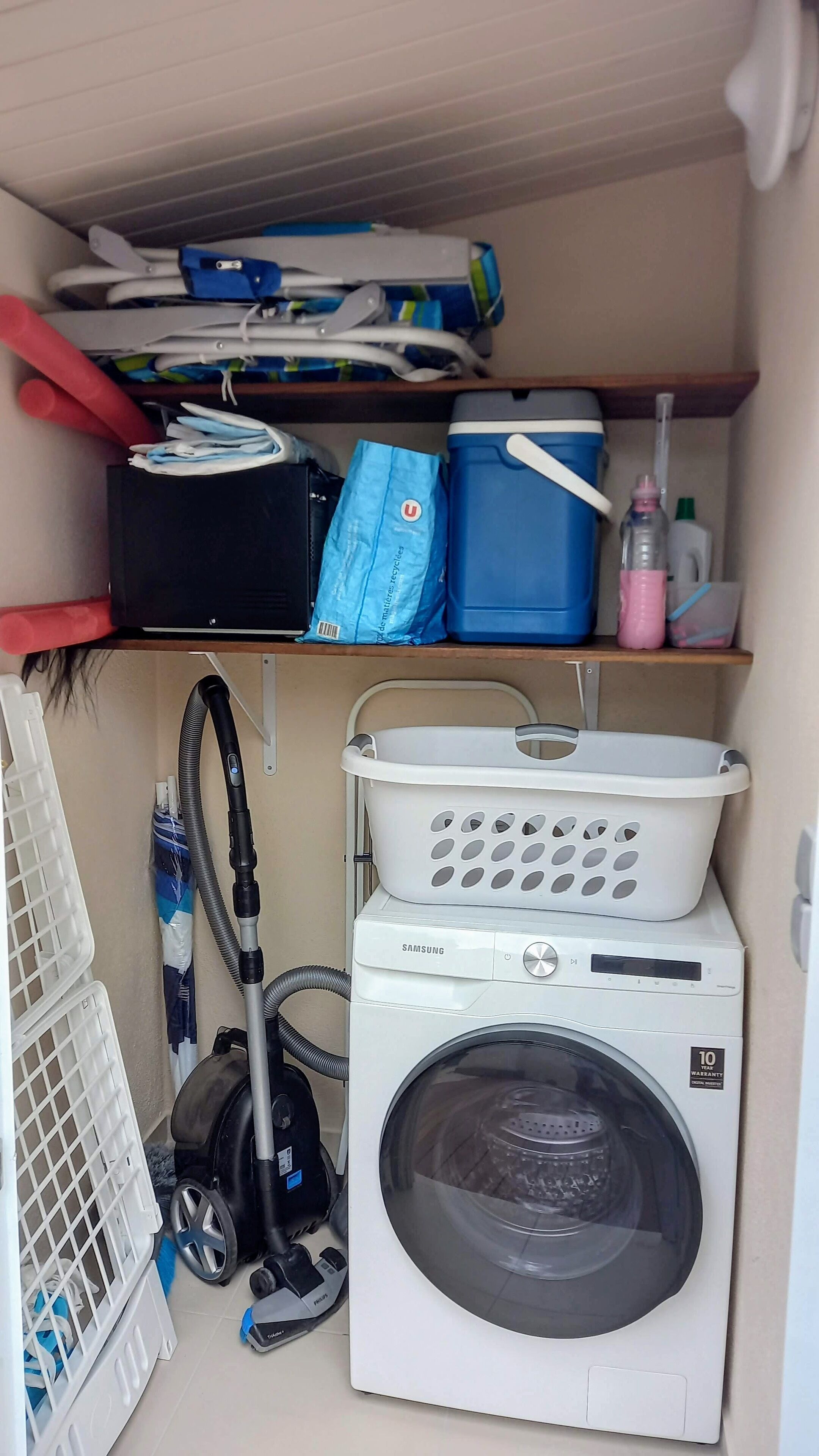 A laundry area with a washing machine, a vacuum cleaner, and various laundry supplies.