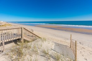 A beach with a wooden boardwalk leading to the water, sandy dunes, and a clear blue sky.