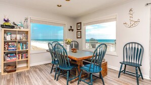 A dining area with a view of the beach, wooden flooring, and a bookshelf with board games. - Sanderling - 4 bedroom, 2.5 Oceanfront Home in North Topsail Beach! (North Topsail Beach)