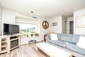 Una sala de estar con televisor de pantalla plana, un sofá azul claro, un mueble de madera y una ventana con vista a edificios.