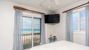 A bedroom with a large bed, a TV mounted on the wall, and a view of the ocean through a sliding glass door. - Sanderling - 4 bedroom, 2.5 Oceanfront Home in North Topsail Beach! (North Topsail Beach)