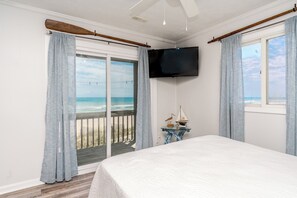 Ein Schlafzimmer mit einem großen Bett, einem an der Wand montierten Fernseher und Blick auf den Ozean durch eine Glastür.