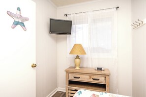 A bedroom with a television mounted on the wall, a bedside lamp, a small wooden nightstand, and a star-shaped welcome sign.