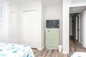 Un dormitori amb un llit, un armari, una televisió a la part superior i un passadís que condueix a una altra habitació.