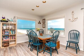 A dining area with a view of the beach, a bookshelf, and a decorative anchor on the wall.