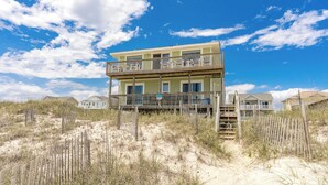 A two-story beachfront property with a balcony, surrounded by sand dunes and sparse vegetation. - Sanderling - 4 bedroom, 2.5 Oceanfront Home in North Topsail Beach! (North Topsail Beach)