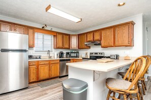 A modern kitchen with wooden cabinets, stainless steel appliances, and a central island with seating. - Sanderling - 4 bedroom, 2.5 Oceanfront Home in North Topsail Beach! (North Topsail Beach)