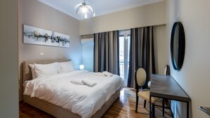 A hotel room with a bed, a desk, a chair, a mirror, and a painting on the wall. - 2br renovated flat close to metro (Athens)