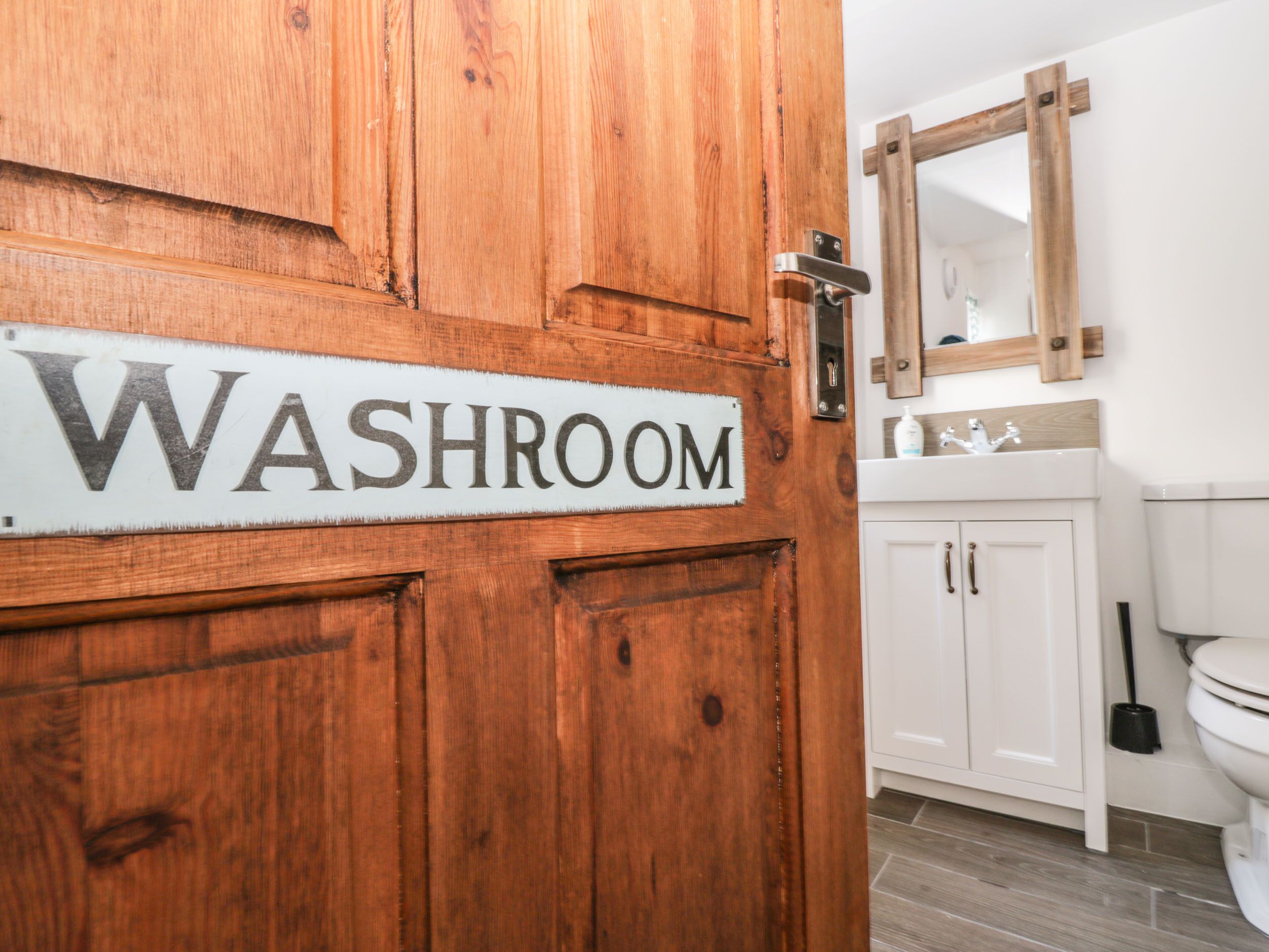 A wooden door with a sign reading "WASHROOM" and a bathroom with a white sink and mirror.