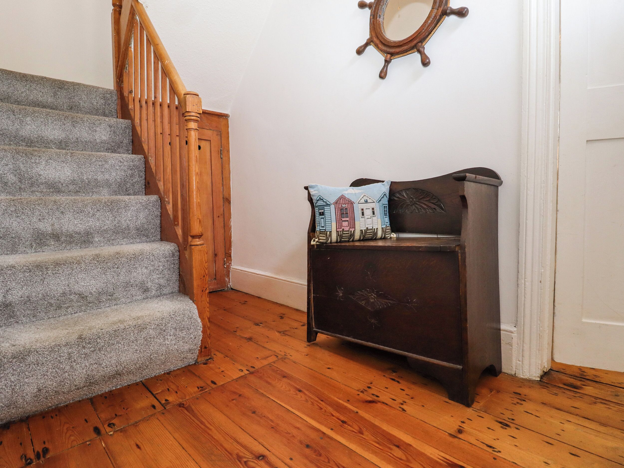 A staircase with wooden steps and a handrail, leading to a landing with a dark wooden bench and a decorative mirror on the wall.