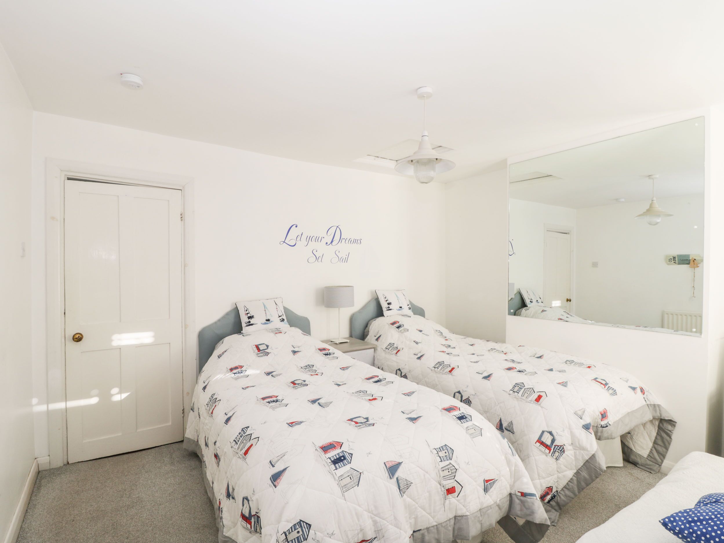 A bedroom with two beds, a ceiling fan, a mirror, and a door.