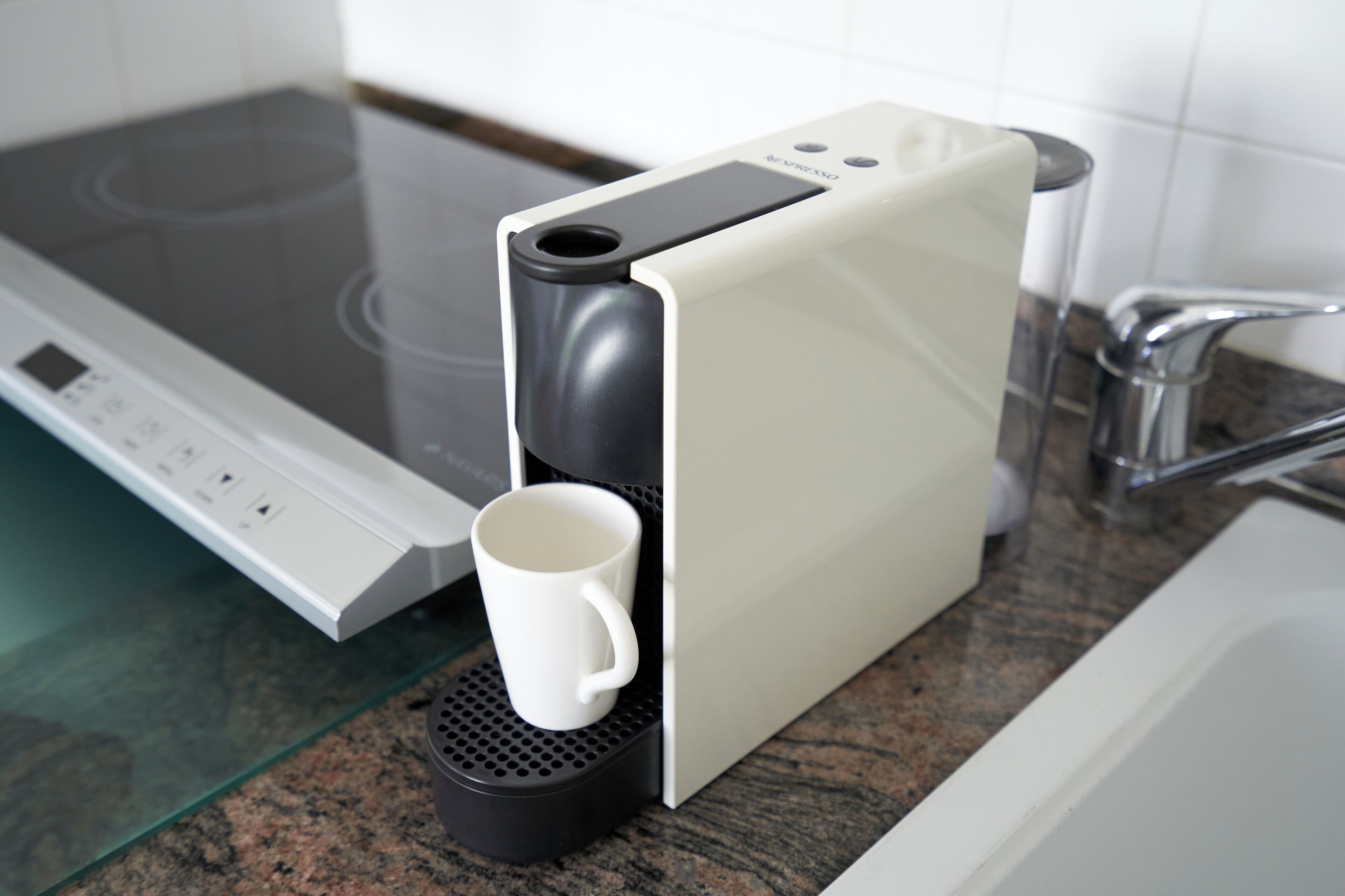 A coffee machine with a white mug on its drip tray, a stovetop, and a kitchen sink.