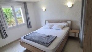 A bedroom with a bed, a nightstand, a wall-mounted light, and a window with curtains. - Apartment near the beach and local shops in a quiet neighborhood (Saint-Cyprien)