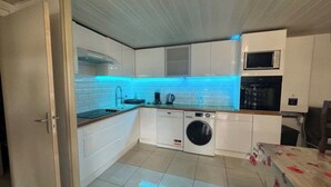 A compact kitchen with white cabinets, a washing machine, and a microwave. - Apartment near the beach and local shops in a quiet neighborhood (Saint-Cyprien)
