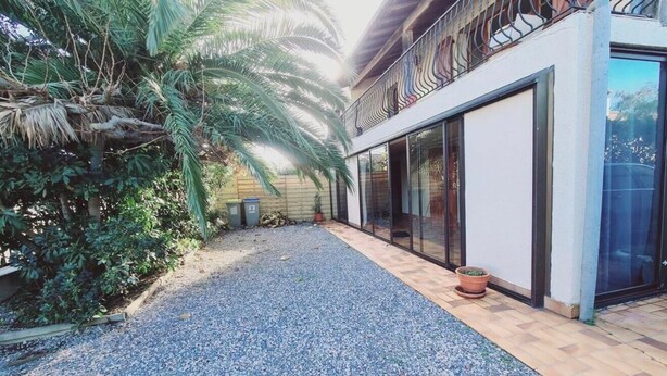 A paved courtyard with a gravel path, a palm tree, and a building with large windows and a balcony. - Apartment near the beach and local shops in a quiet neighborhood (Saint-Cyprien)