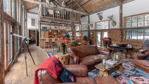 Interior rústico de una cabaña con vigas de madera, mobiliario de cuero y trofeos de animales.