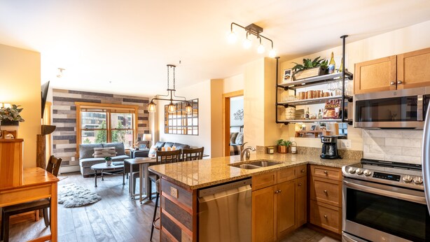 A modern kitchen with a central island, stainless steel appliances, and a dining area with a sofa and chairs. - Steps away from Super Bee Lift, wifi, underground parking (Copper Mountain)