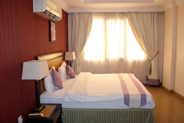 A hotel room with a bed, a nightstand, a lamp, a remote control, and a window with curtains.